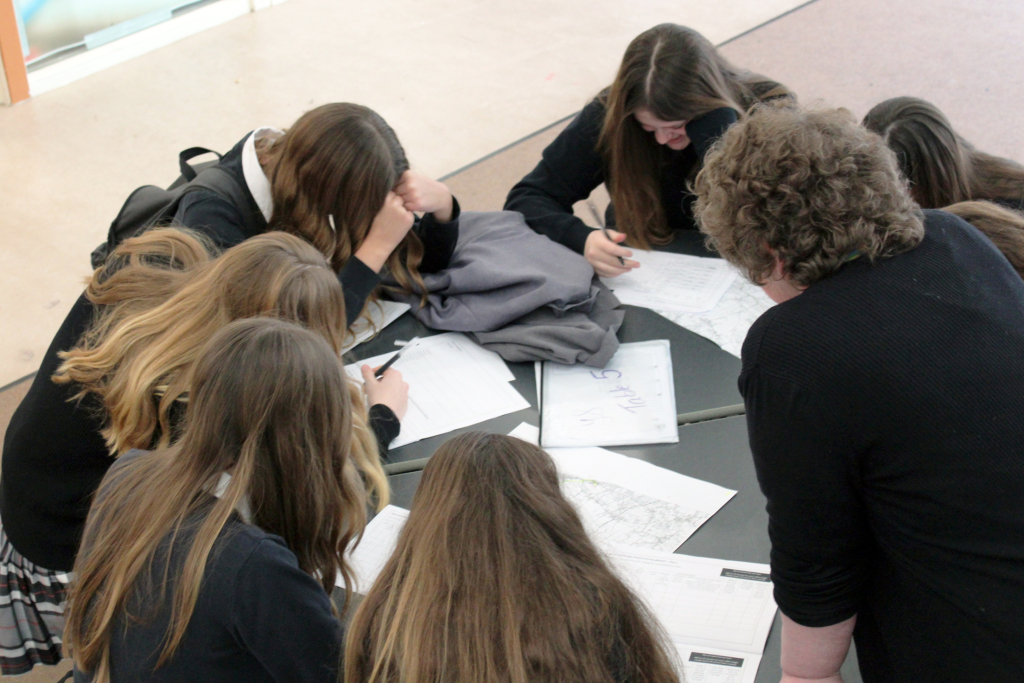 A Sixth Form Student Leader works with a group of younger students to plan routes for the Duke of Edinburgh Award walks. The students are working on planners and using ordinance survey maps.